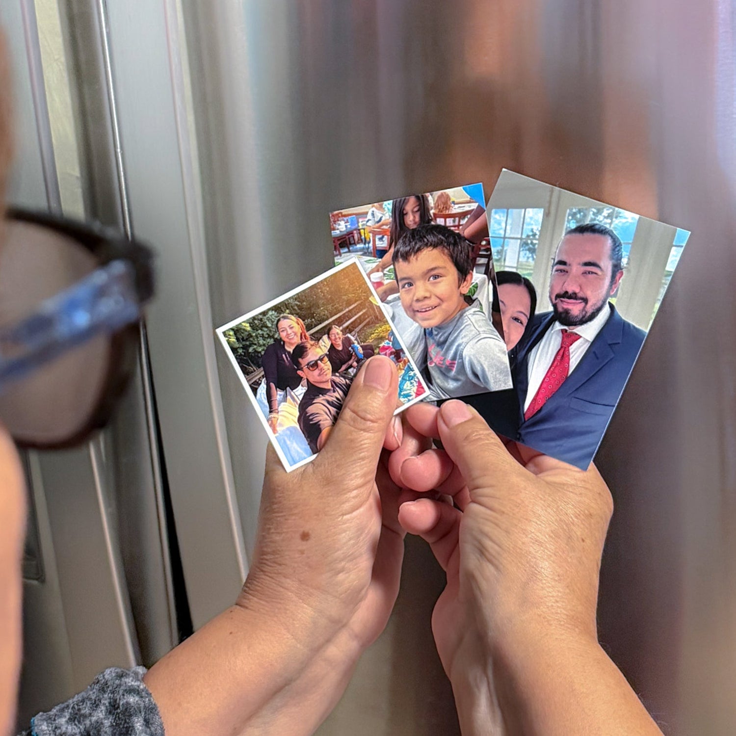 Hands holding 3 sizes of photo flexible magnets in front of a metallic refrigerator.